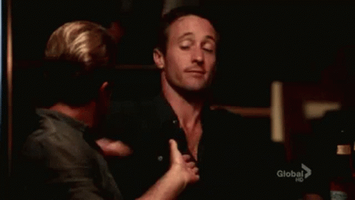 Two Men Are Hugging Each Other In A Dark Room And One Of Them Is Waving At The Camera . GIF