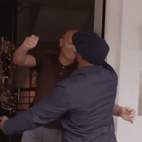 Two Men Are Hugging Each Other In A Room And One Of Them Is Wearing A Blue Hat . GIF