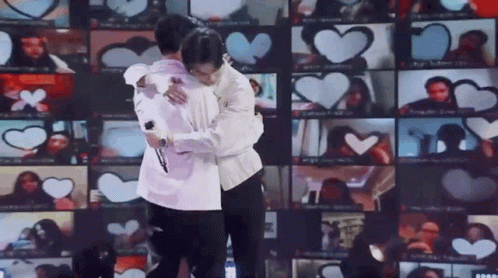 Two Men Are Hugging Each Other In Front Of A Wall Of Hearts . GIF