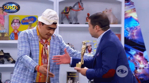 Two Men Are Hugging In Front Of A Sign That Says Susos GIF