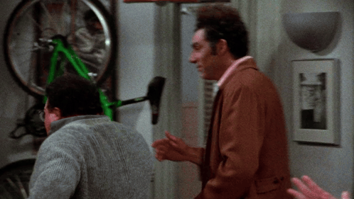Two Men Are Looking At A Green Bicycle That Is Hanging On A Wall GIF