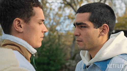 Two Men Are Looking At Each Other And One Has A Netflix Logo On His Shirt GIF