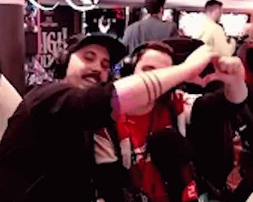 Two Men Are Making A Heart Shape With Their Hands While Sitting Next To Each Other . GIF