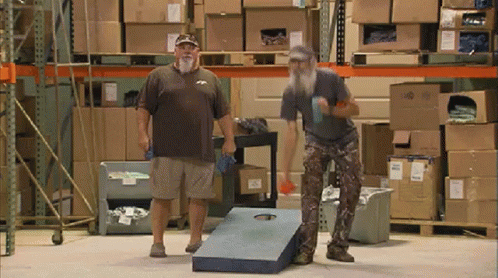 Two Men Are Playing A Game In A Warehouse With Boxes On The Shelves GIF