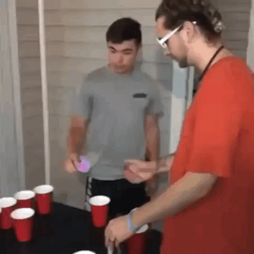 Two Men Are Playing A Game Of Beer Pong With Red Cups On The Table . GIF