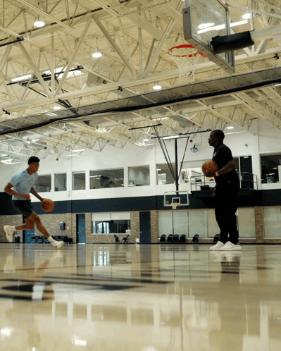 Two Men Are Playing Basketball In A Gym With A Hoop In The Background GIF