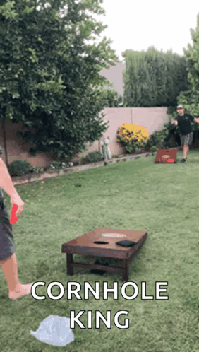 Two Men Are Playing Cornhole In A Backyard With The Caption " Cornhole King " On The Bottom GIF