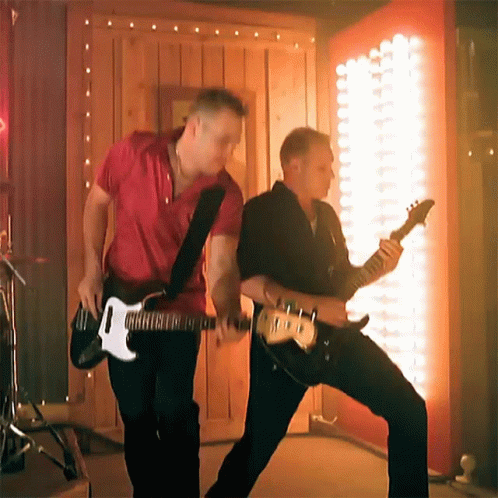 two men are playing guitars in front of a wall with lights