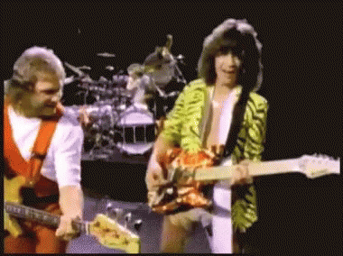 Two Men Are Playing Guitars On A Stage With A Drum Set In The Background GIF