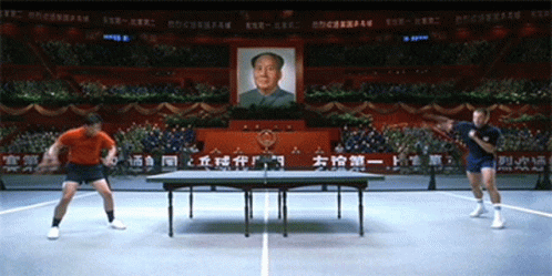 Two Men Are Playing Ping Pong In Front Of A Picture Of Mao Zedong On The Wall GIF