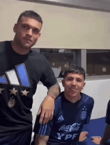 Two Men Are Posing For A Picture And One Has A Coca Cola Shirt On GIF
