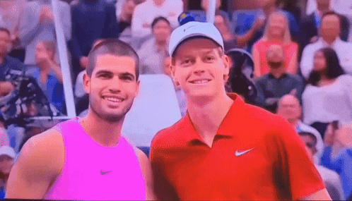 two men are posing for a picture in front of a crowd . one is wearing a pink tank top .