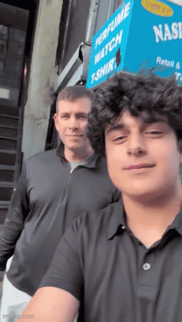 two men are posing for a picture in front of a perfume watch t-shirt store