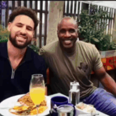 Two Men Are Posing For A Picture While Sitting At A Table With Food And Drinks GIF