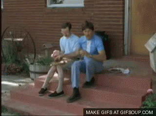 Two Men Are Riding A Bicycle On A Dirt Road With Mountains In The Background GIF