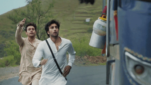 Two Men Are Running Down A Road And One Has A Bag On His Shoulder GIF