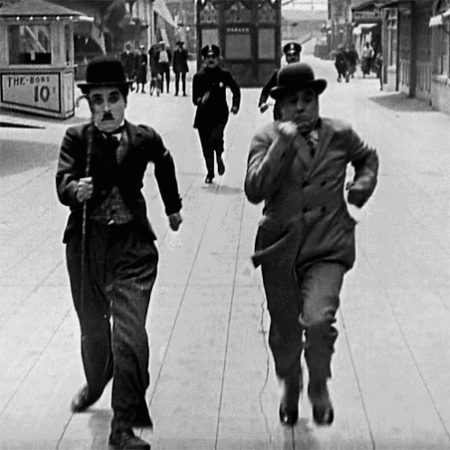 Two Men Are Running Down A Street In Front Of A Sign That Says The Boss 10 Cents GIF