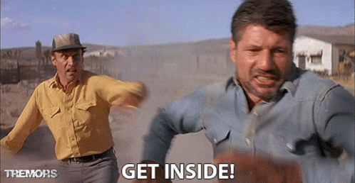 Two Men Are Running In A Dirt Field And One Of Them Is Saying Get Inside GIF