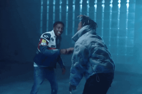 Two Men Are Shaking Hands In A Dark Room And One Has A Jacket That Says ' Audi ' On The Back GIF