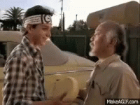 Two Men Are Shaking Hands In Front Of A Car . One Of The Men Is Wearing A Headband With The Letter G On It . GIF