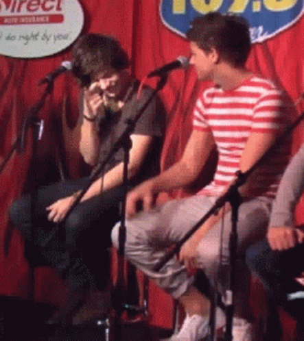 Two Men Are Singing Into Microphones In Front Of A Sign That Says 102.9 GIF
