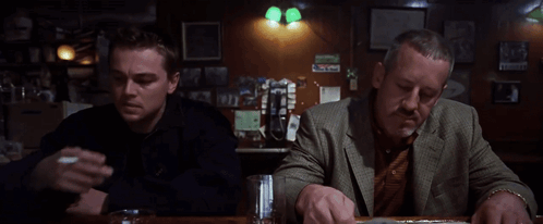 Two Men Are Sitting At A Bar Smoking Cigarettes And Drinking Beer GIF