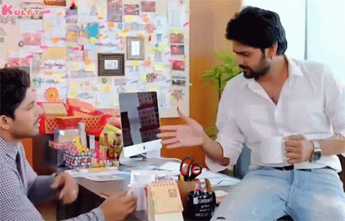 Two Men Are Sitting At A Desk In Front Of A Computer And Talking . GIF