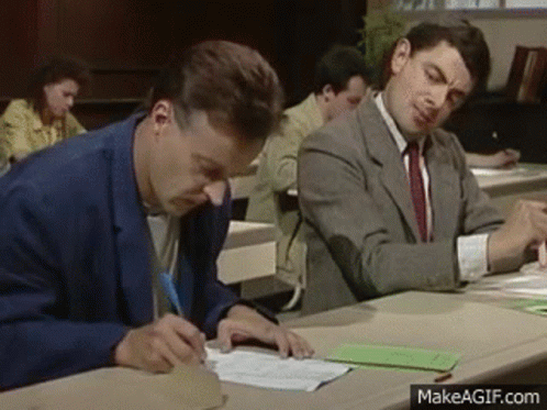 Two Men Are Sitting At A Desk Writing On A Piece Of Paper In A Classroom . GIF