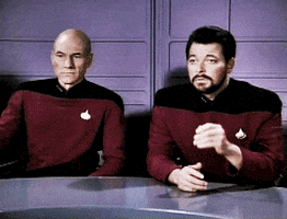 Two Men Are Sitting At A Table And One Has A Badge On His Shirt That Says ' Captain ' GIF