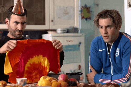 Two Men Are Sitting At A Table And One Is Wearing A Blue Nike Jacket GIF