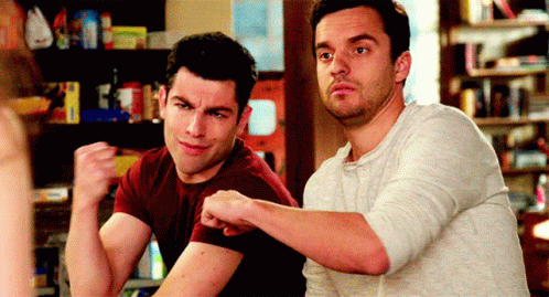 Two Men Are Sitting At A Table And One Of Them Is Flexing His Arms GIF