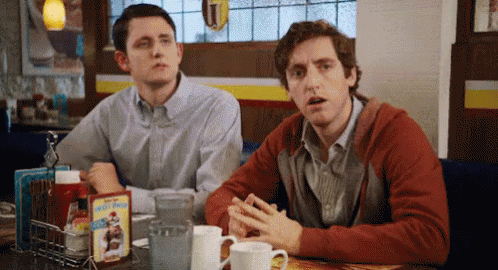Two Men Are Sitting At A Table In A Diner With A Box Of Kellogg 'S Cereal On It GIF