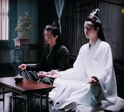 Two Men Are Sitting At A Table In A Room . One Of The Men Is Wearing A White Robe . GIF