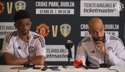 Two Men Are Sitting At A Table In Front Of A Sign That Says Ticketmaster GIF