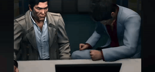 two men are sitting at a table looking at a computer screen .