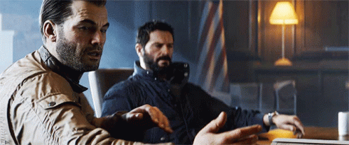 Two Men Are Sitting At A Table Looking At A Laptop Computer GIF