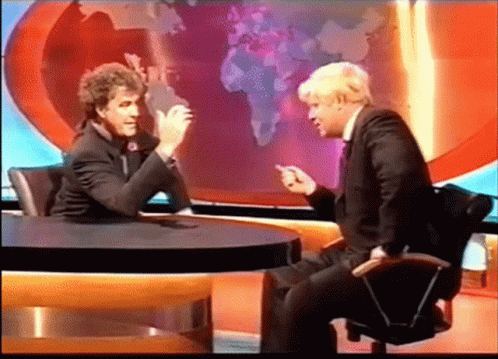 Two Men Are Sitting At A Table Talking In Front Of A World Map GIF