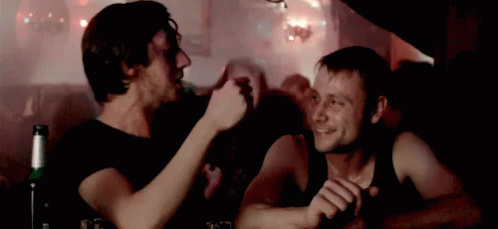 Two Men Are Sitting At A Table With A Bottle Of Beer In The Foreground . GIF