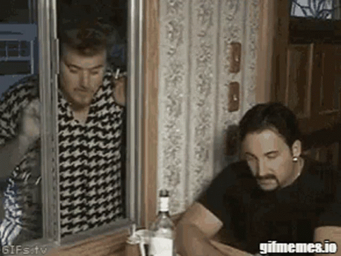 Two Men Are Sitting At A Table With A Bottle Of Vodka And Talking On A Cell Phone . GIF