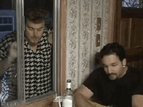 Two Men Are Sitting At A Table With A Bottle Of Vodka In Front Of Them And One Of Them Is Smoking A Cigarette . GIF