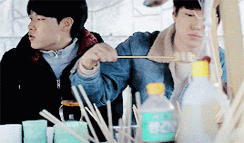 Two Men Are Sitting At A Table With A Bottle That Says 820 GIF
