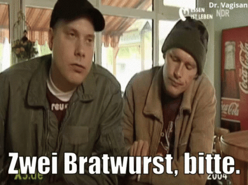 Two Men Are Sitting At A Table With A Coca Cola Fridge In The Background GIF