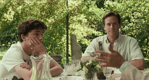 Two Men Are Sitting At A Table With A Pitcher Of Water GIF