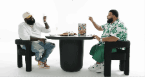 Two Men Are Sitting At A Table With A Pizza On It GIF