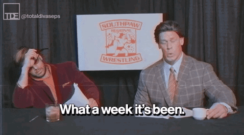 Two Men Are Sitting At A Table With A Sign That Says Southpaw Regional Wrestling GIF