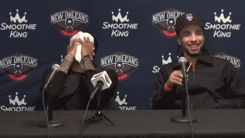 Two Men Are Sitting At A Table With Microphones In Front Of Smoothie King Advertisements GIF