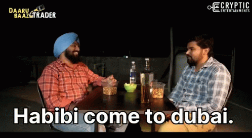 Two Men Are Sitting At A Table With The Words Habibi Come To Dubai On The Screen GIF