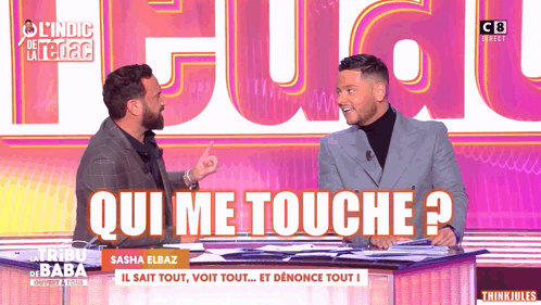 Two Men Are Sitting At A Table With The Words Qui Me Touche On The Screen Behind Them GIF