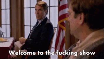 Two Men Are Sitting At A Table With The Words Welcome To The Fucking Show Written On The Screen . GIF