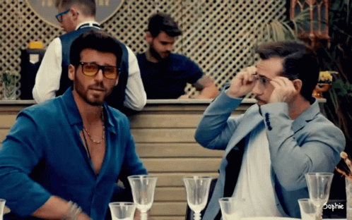 Two Men Are Sitting At A Table With Wine Glasses And The Word Sophie On The Bottom GIF